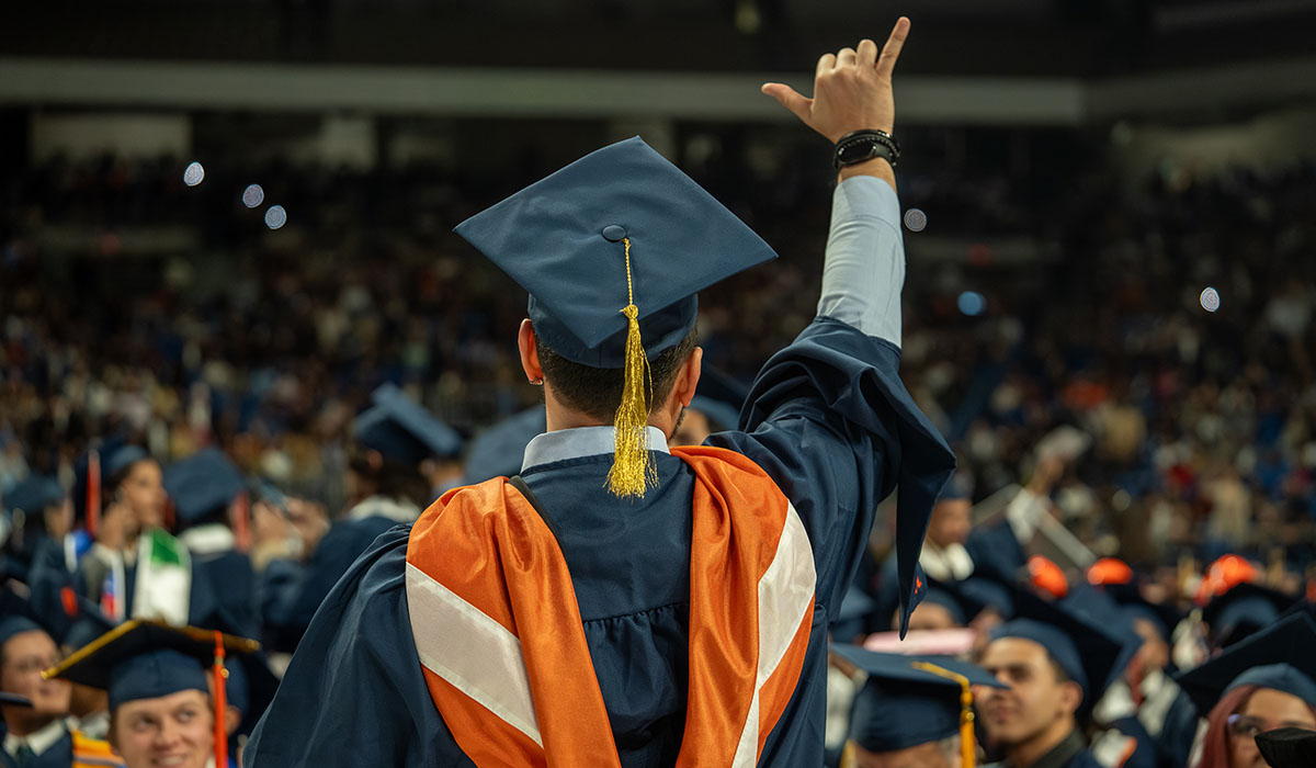 A UT San Antonio master's graduate making the birds up hand symbol 