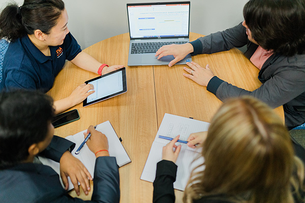 Four students sitting at a table studying and looking at a laptop screen