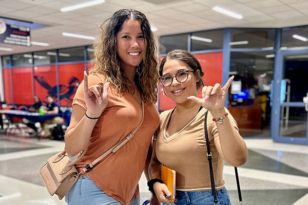 Two students smiling and doing the roadrunner sign with their hands