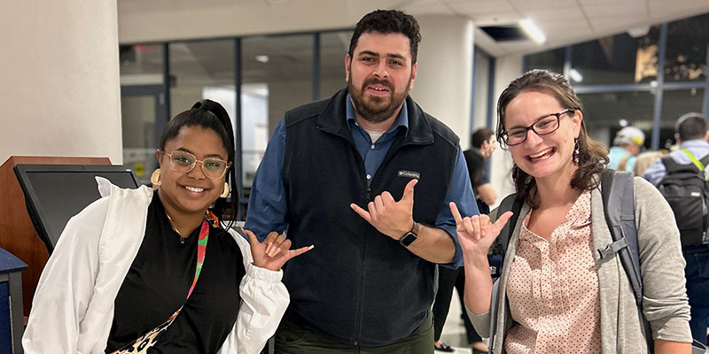 Three students smiling and doing the roadrunner sign with their hands