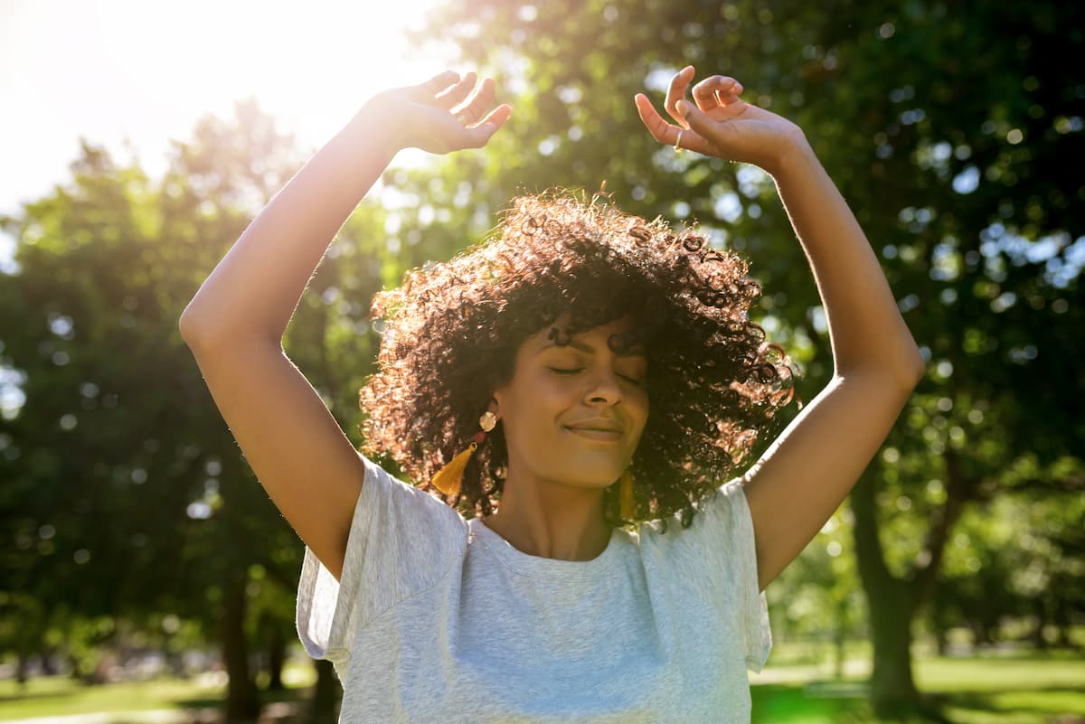 Woman lifting hands while outside with sun shining from behind